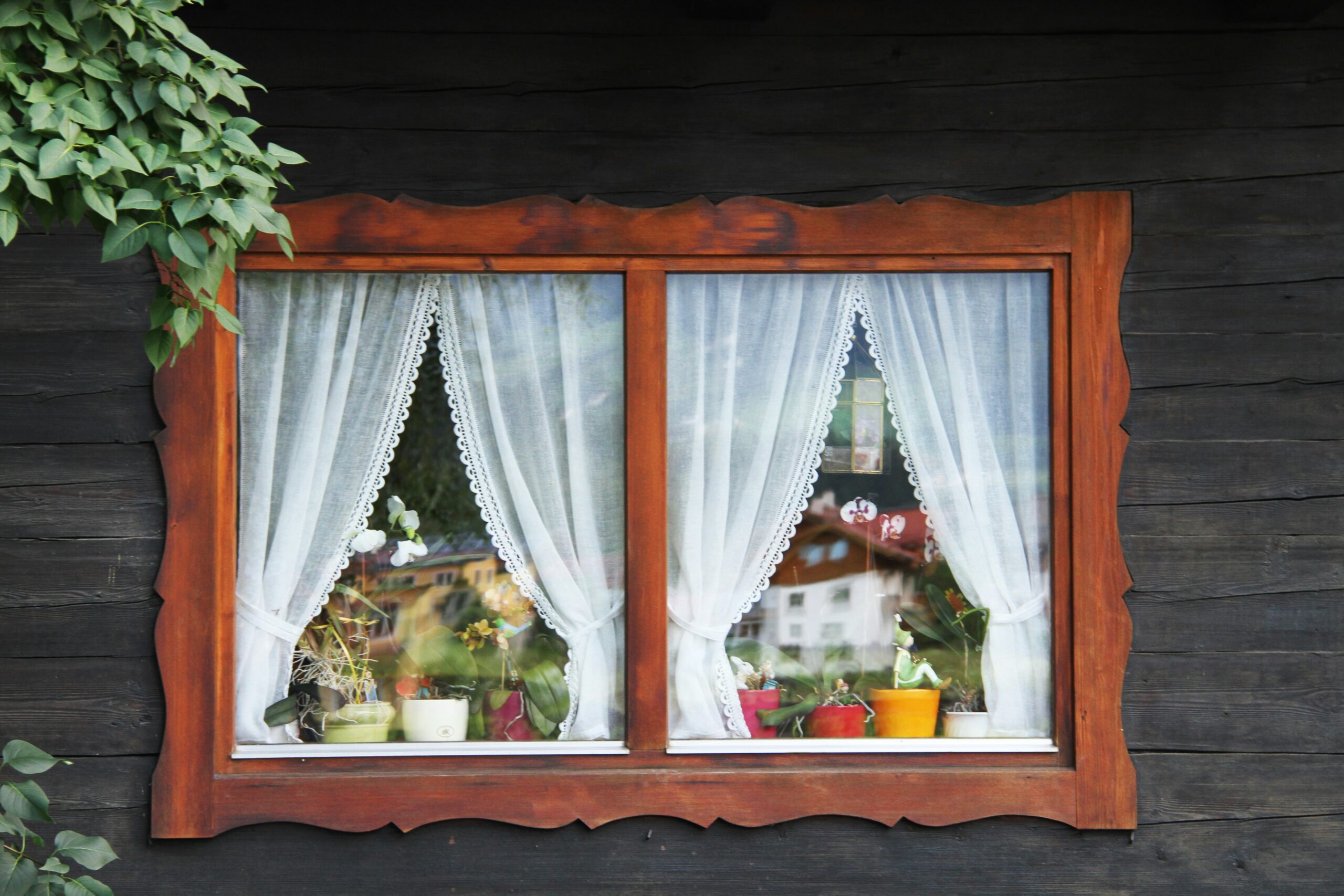 Kleines Doppelfenster mit Gardinen und Blumen im Fenster